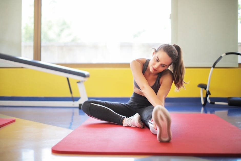 Female athlete stretching on a red yoga mat indoors, emphasizing flexibility and fitness.